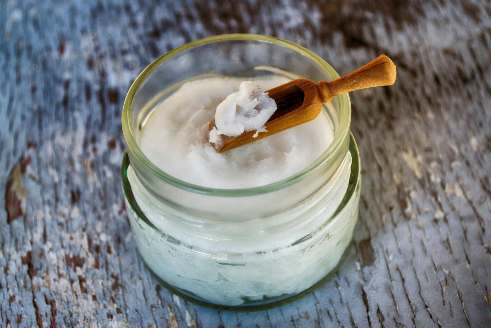 Close-up of organic coconut oil in glass jar with wooden spoon, perfect for natural health and wellness use.